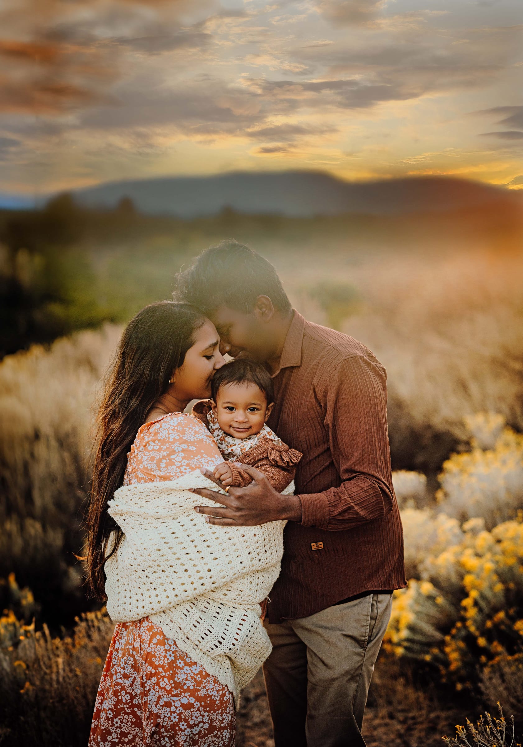 Parents holding their young child close in warm evening light
