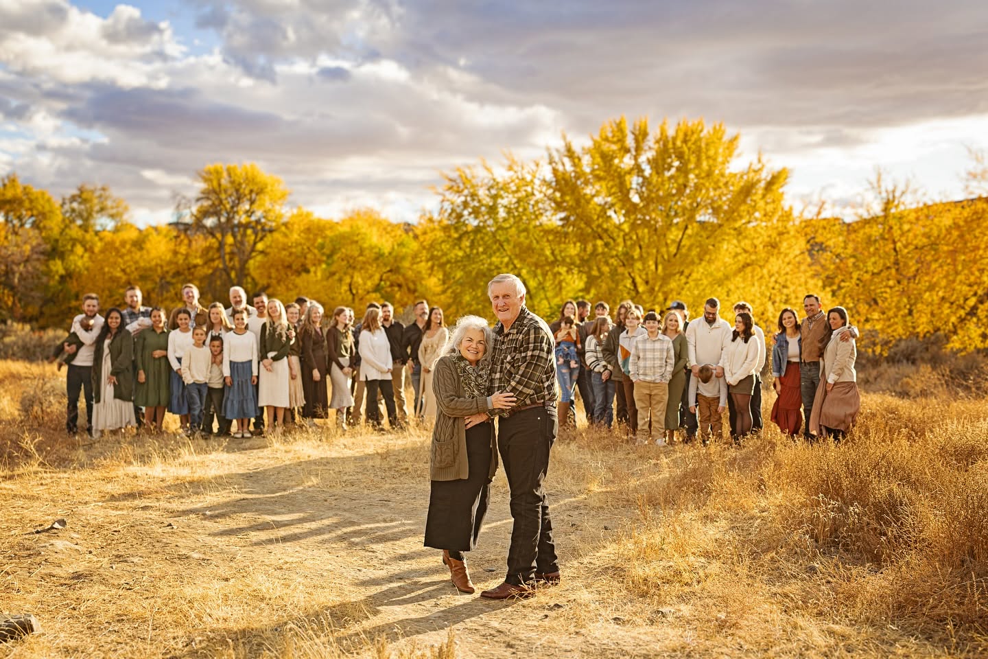 A large extended family gathered outdoors beneath golden autumn trees