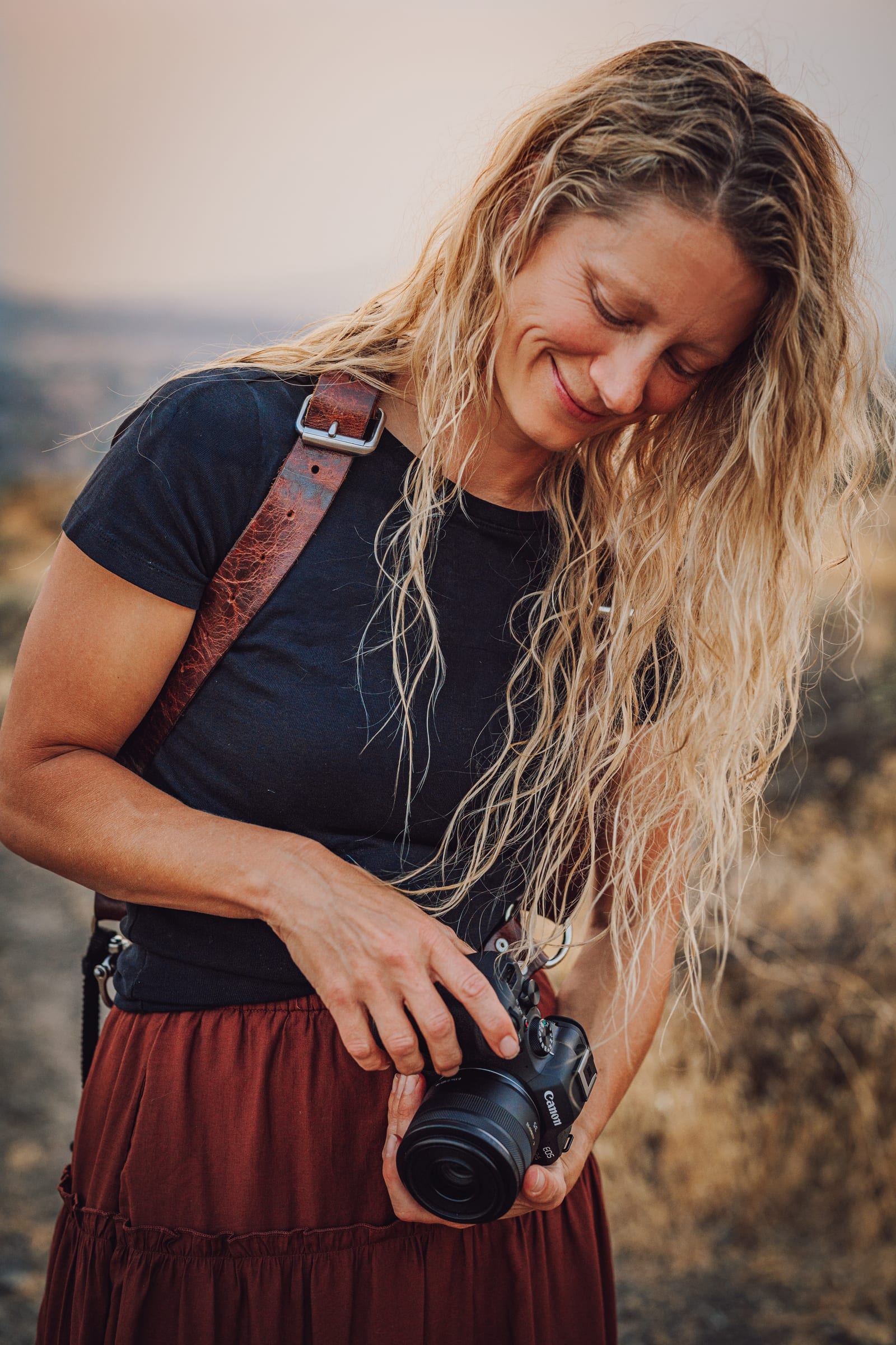 Close portrait of Lisa looking down as she adjusts a camera outdoors.