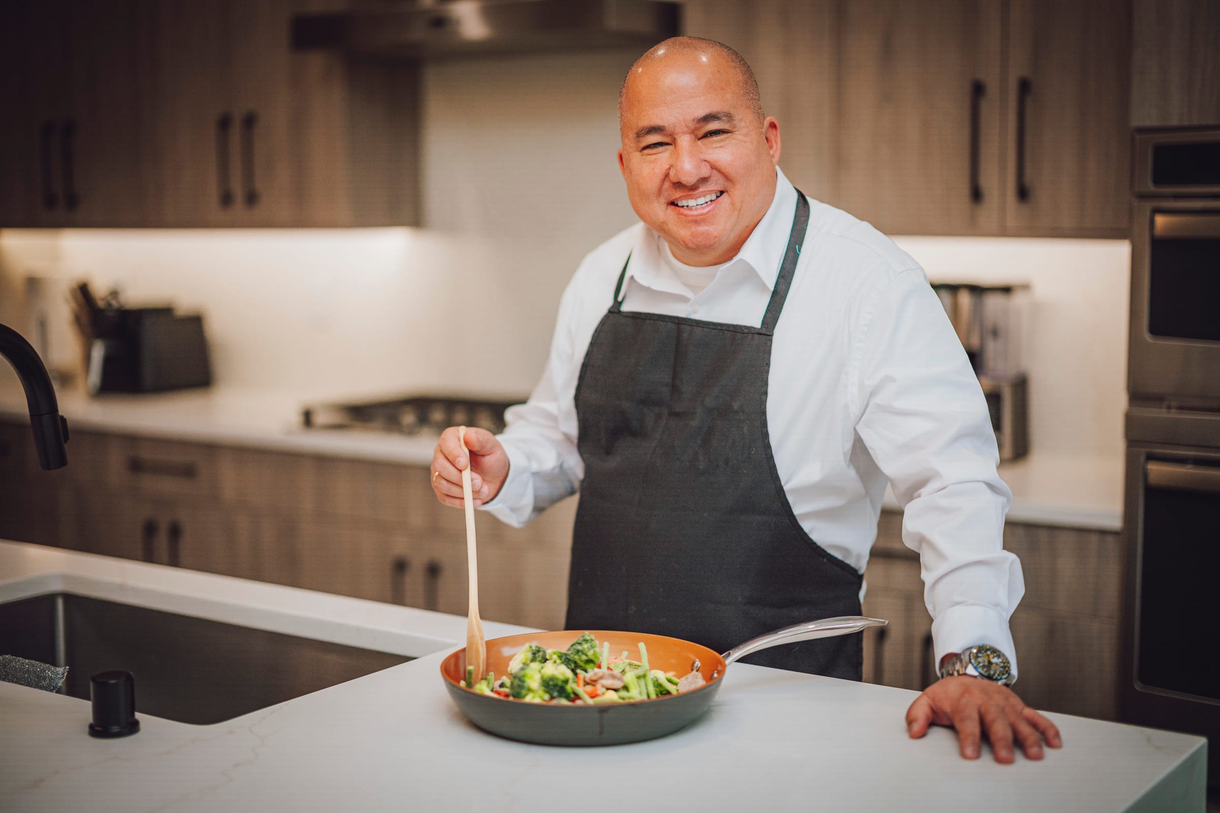 Chef smiling while stirring vegetables in a modern kitchen during a Richland branding session.