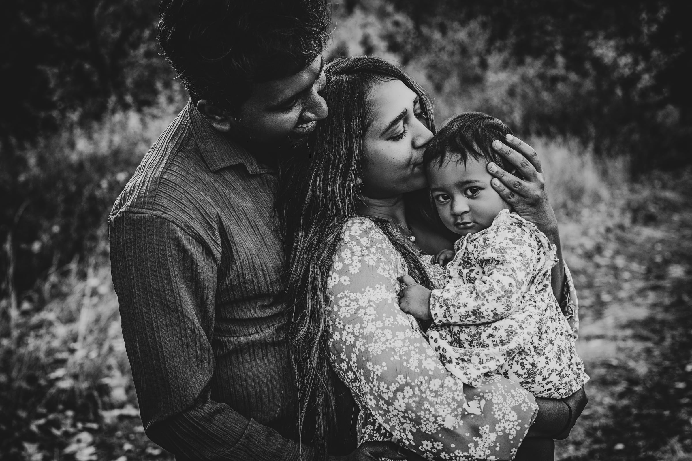 Parents embracing their growing baby in a black-and-white family portrait