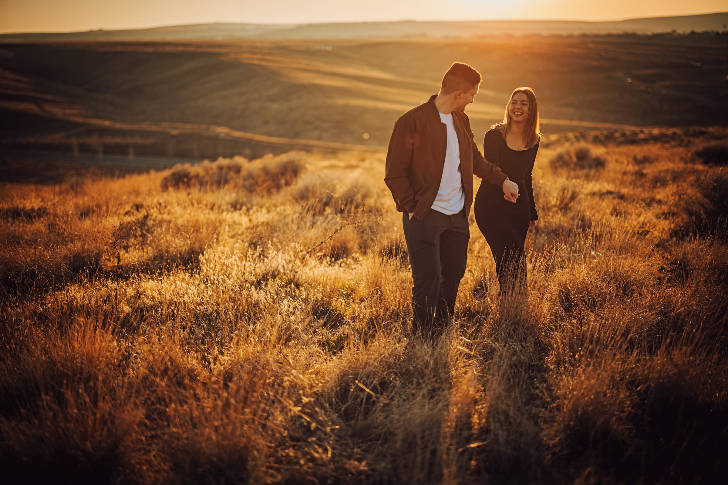 A couple laughing together while walking through an open field in warm evening light