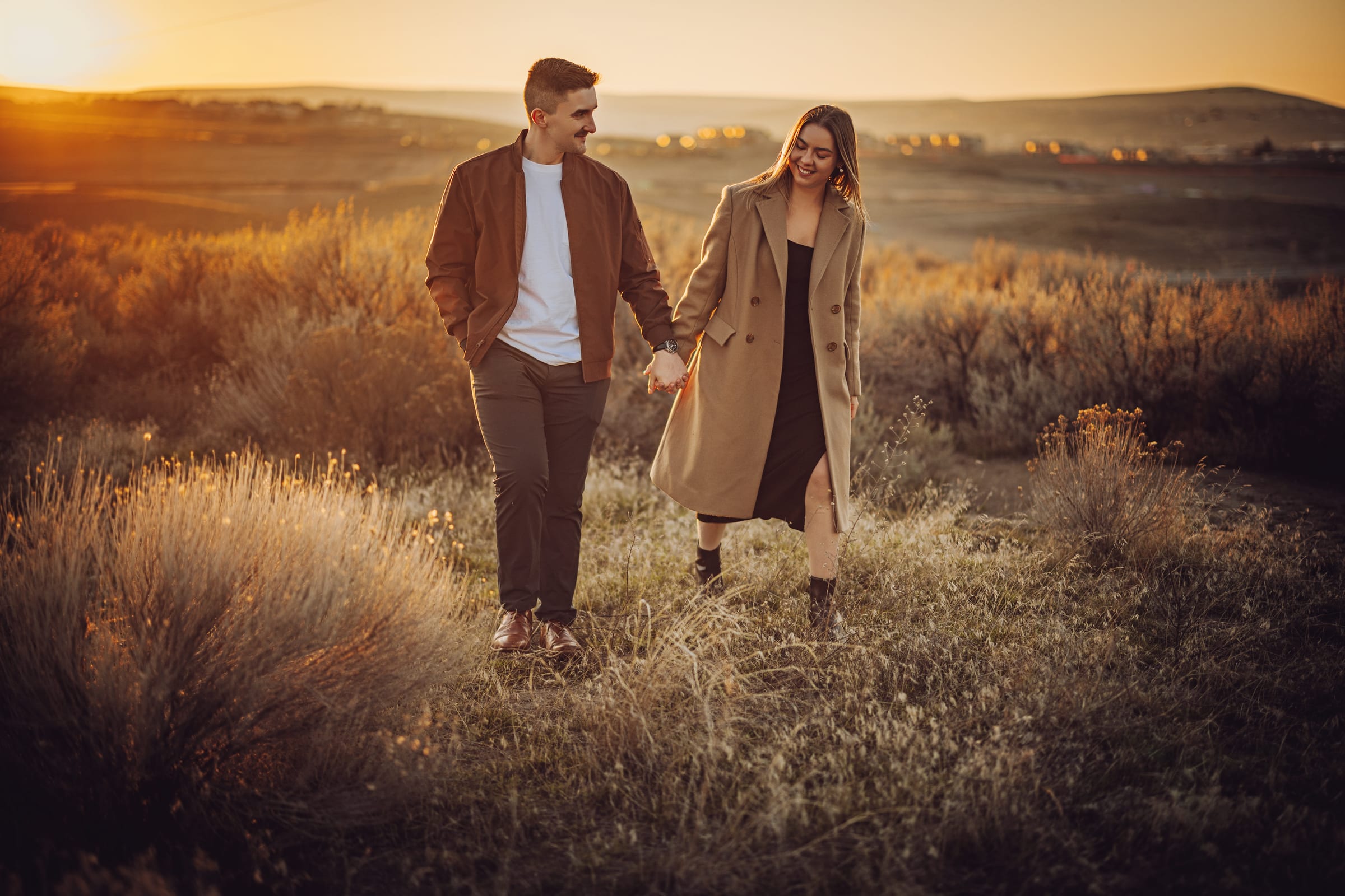 A couple holding hands while walking through a sunlit field.