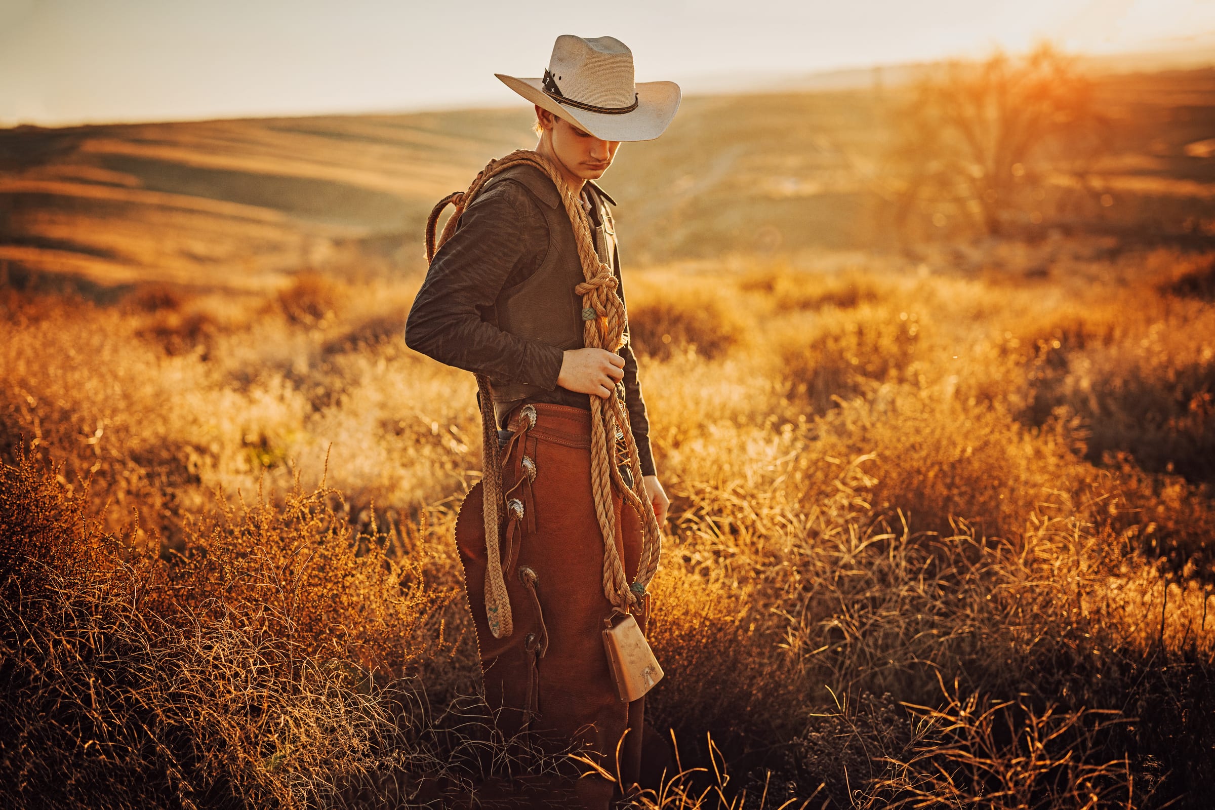 A senior wearing a cowboy hat and holding a rope in warm evening light.