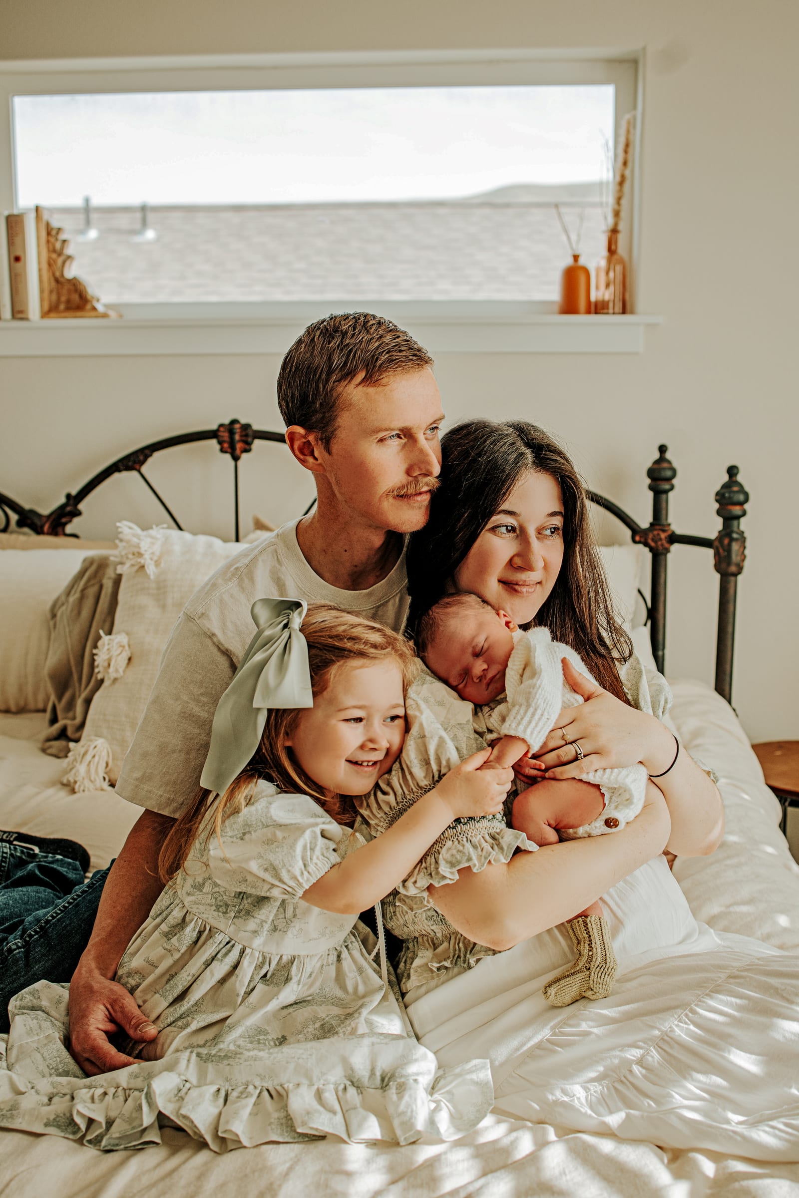 Parents and an older sister gathered around a sleeping newborn on a bed