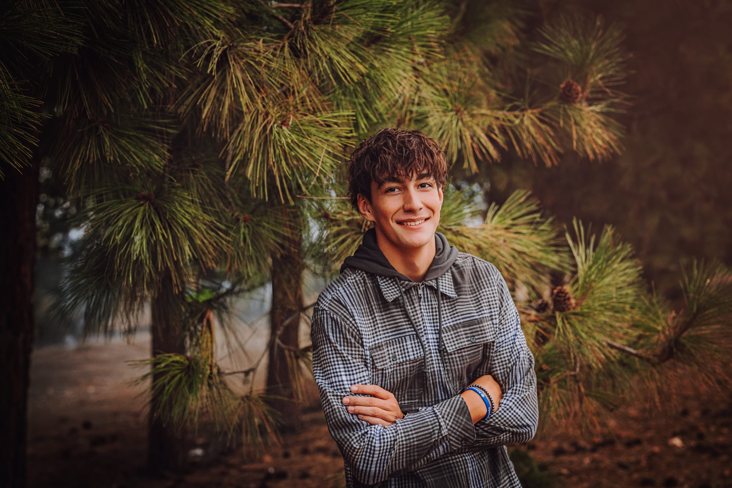 High school senior smiling in front of green pine branches.