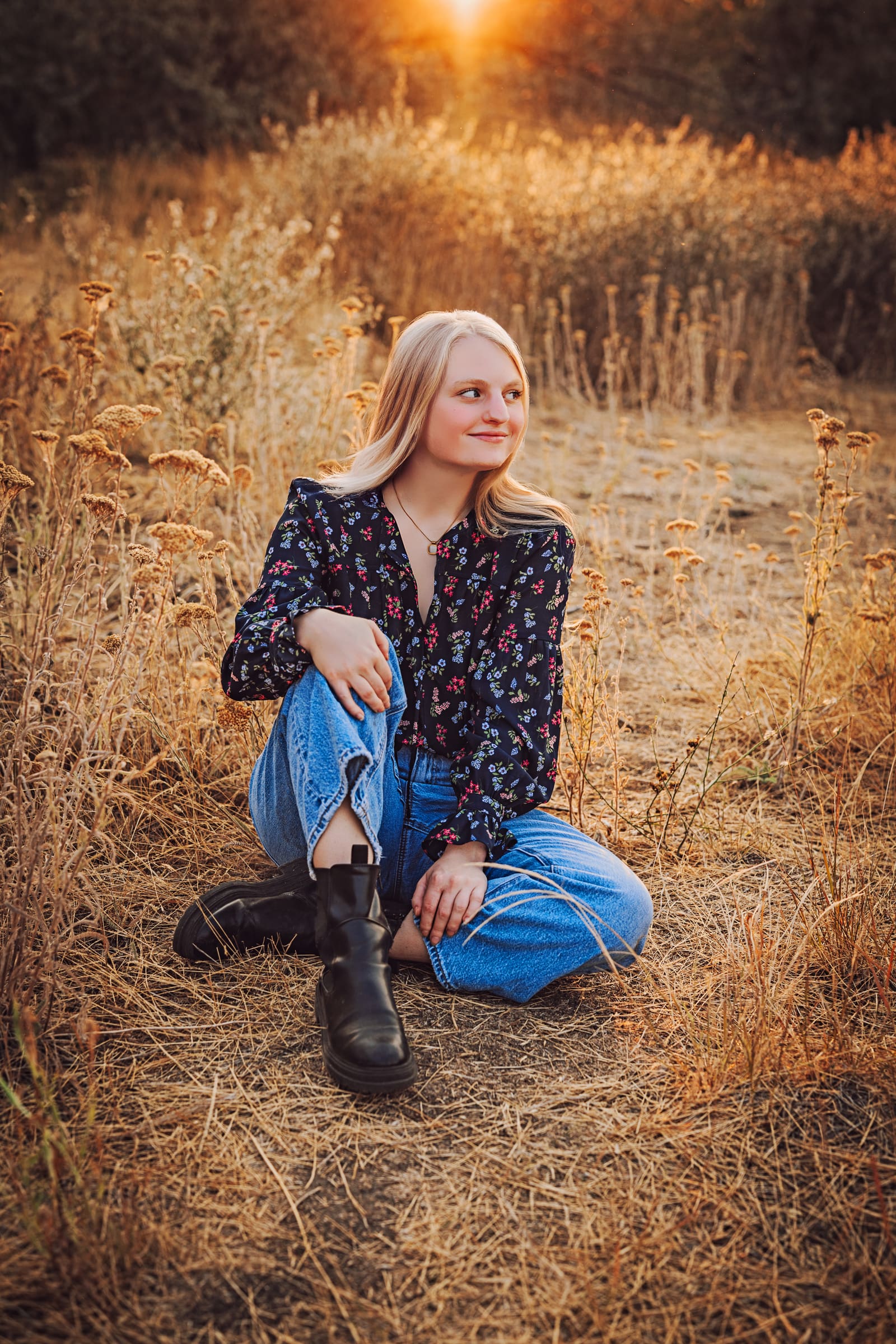 High school senior seated among dry wildflowers in warm evening light.