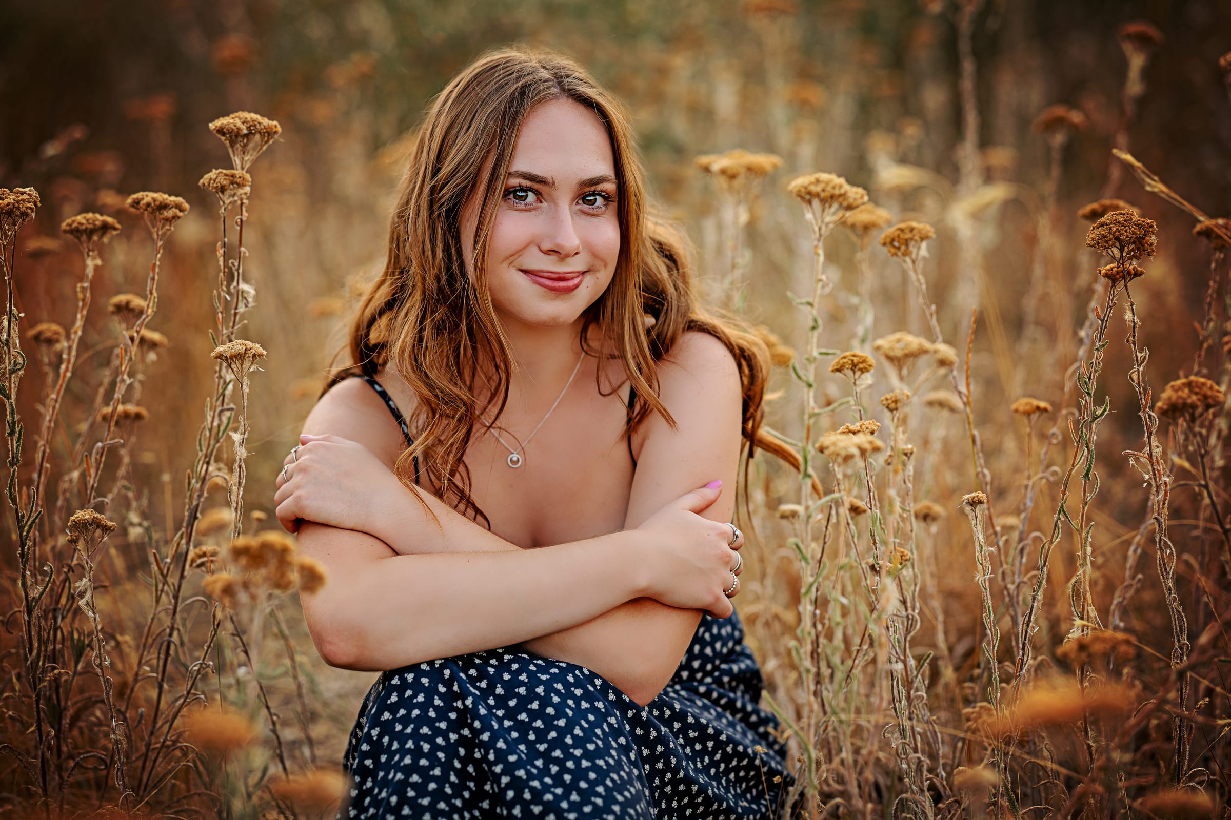High school senior seated among dry wildflowers in warm light.