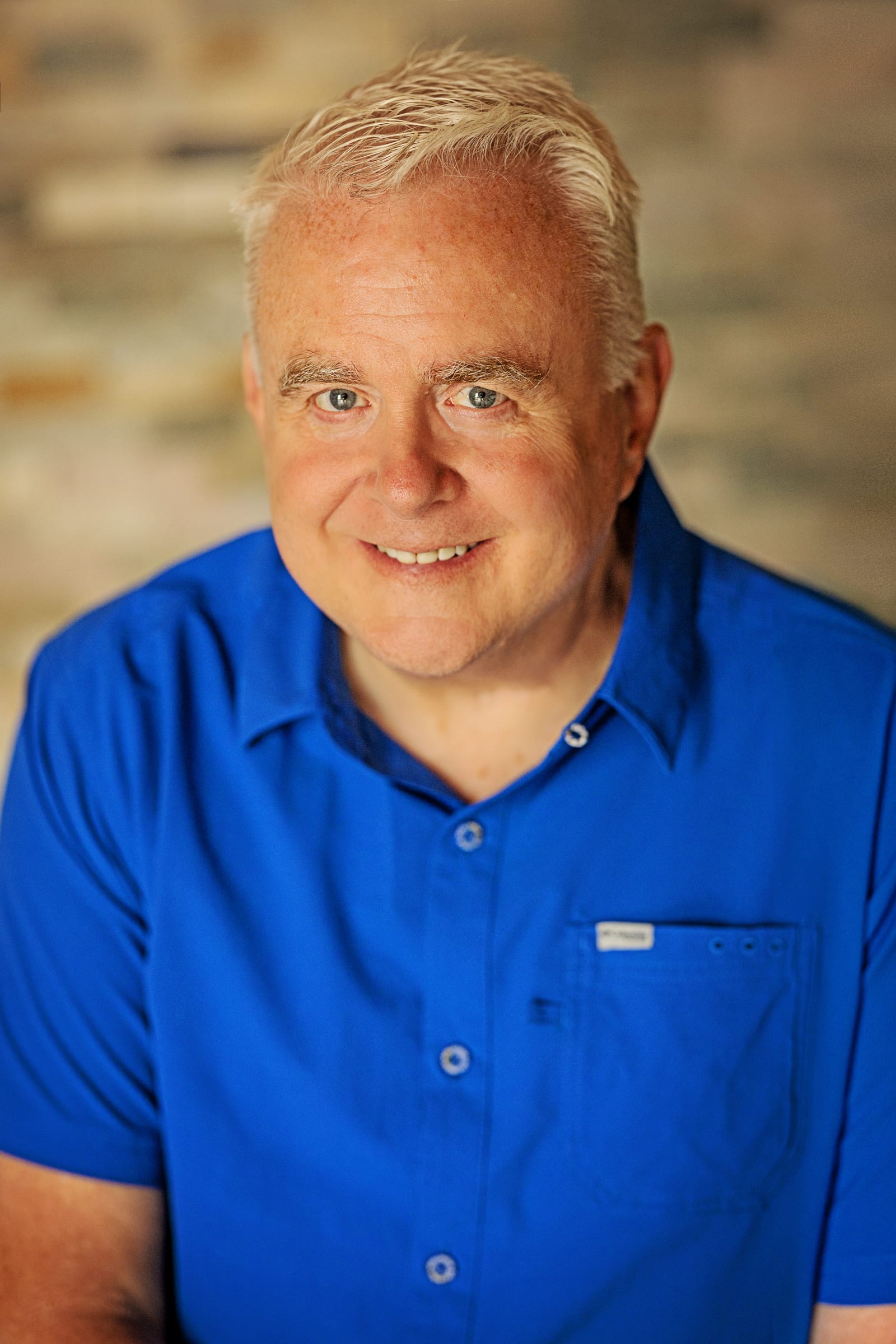 Smiling man in a blue shirt photographed against a warm stone backdrop in Kennewick.