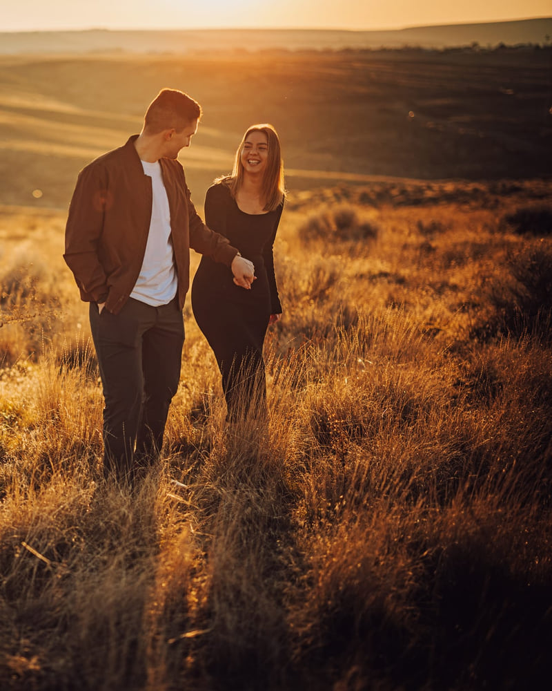 A couple in black clothing walking hand in hand through a golden field