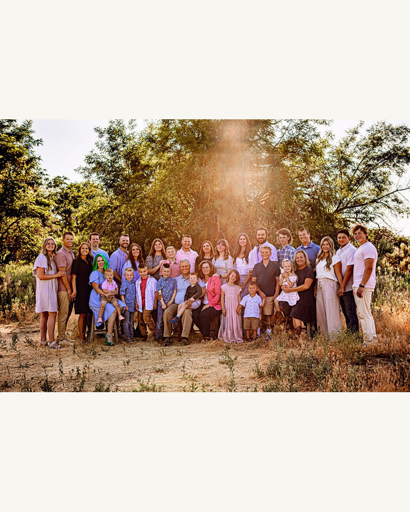 A large extended family gathered outdoors beneath trees
