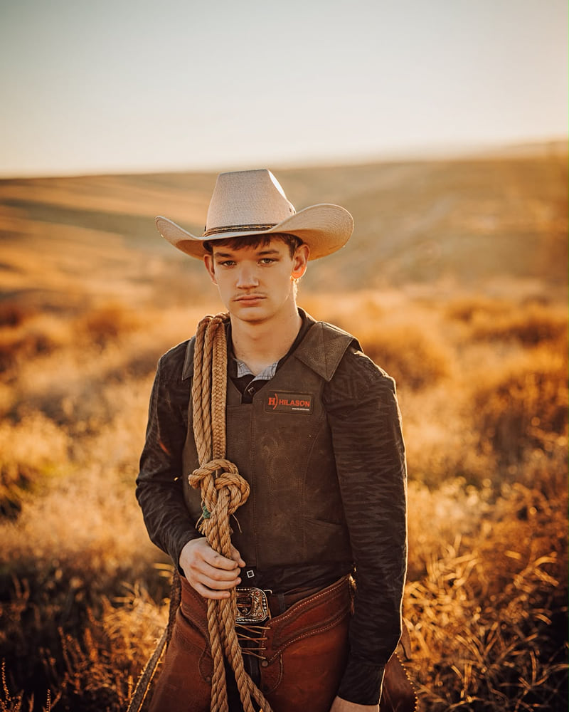 A young cowboy holding a coiled rope in a sunlit field