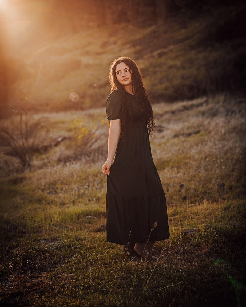 A young woman in a long black dress standing in warm evening light