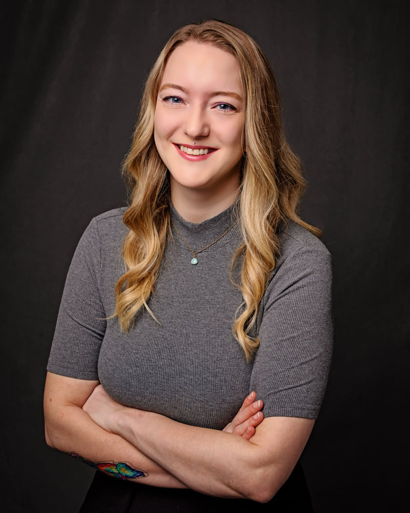 A woman in a gray top smiling with her arms crossed against a dark studio backdrop