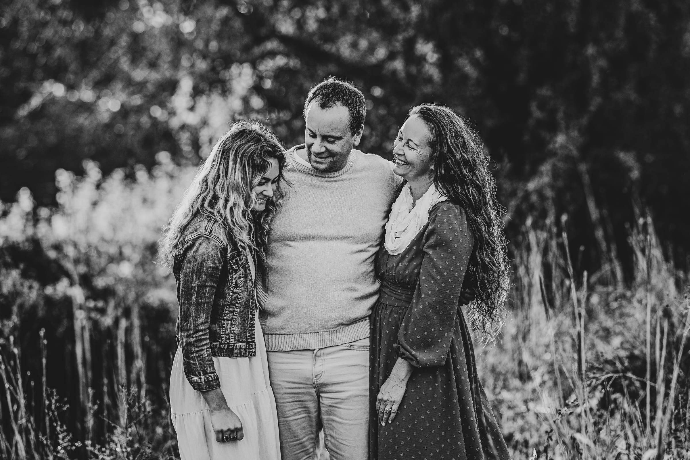 Family of three standing together in a field in a black-and-white portrait.