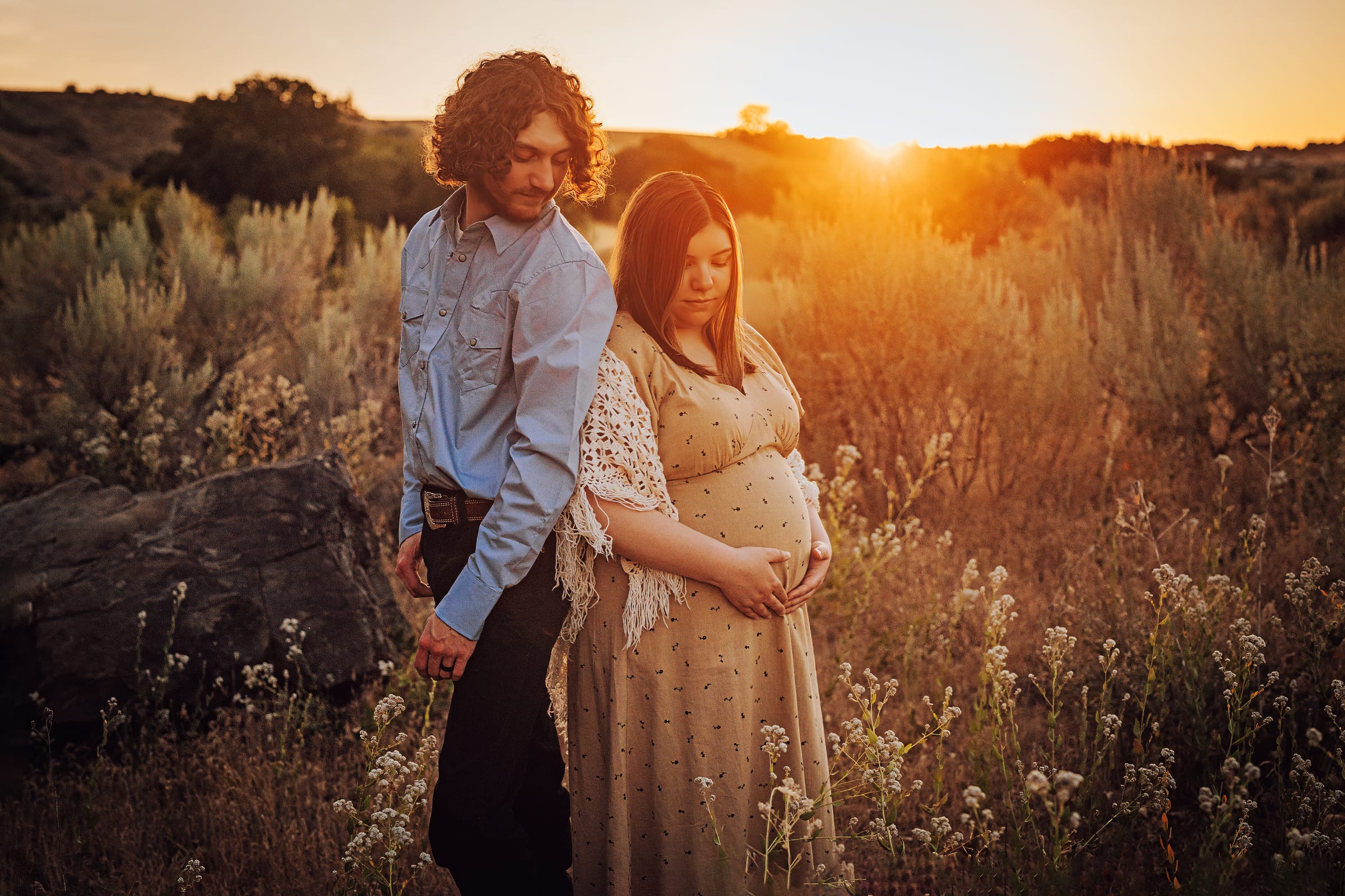 Expectant couple standing together in a sunlit field.